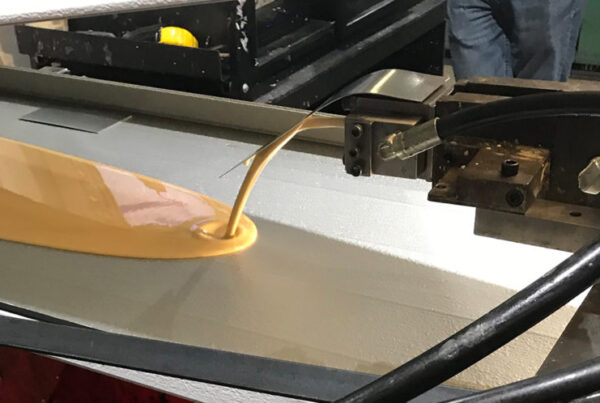 A picture showing the dispensing of foam onto a garage door shell during garage door panel manufacturing.