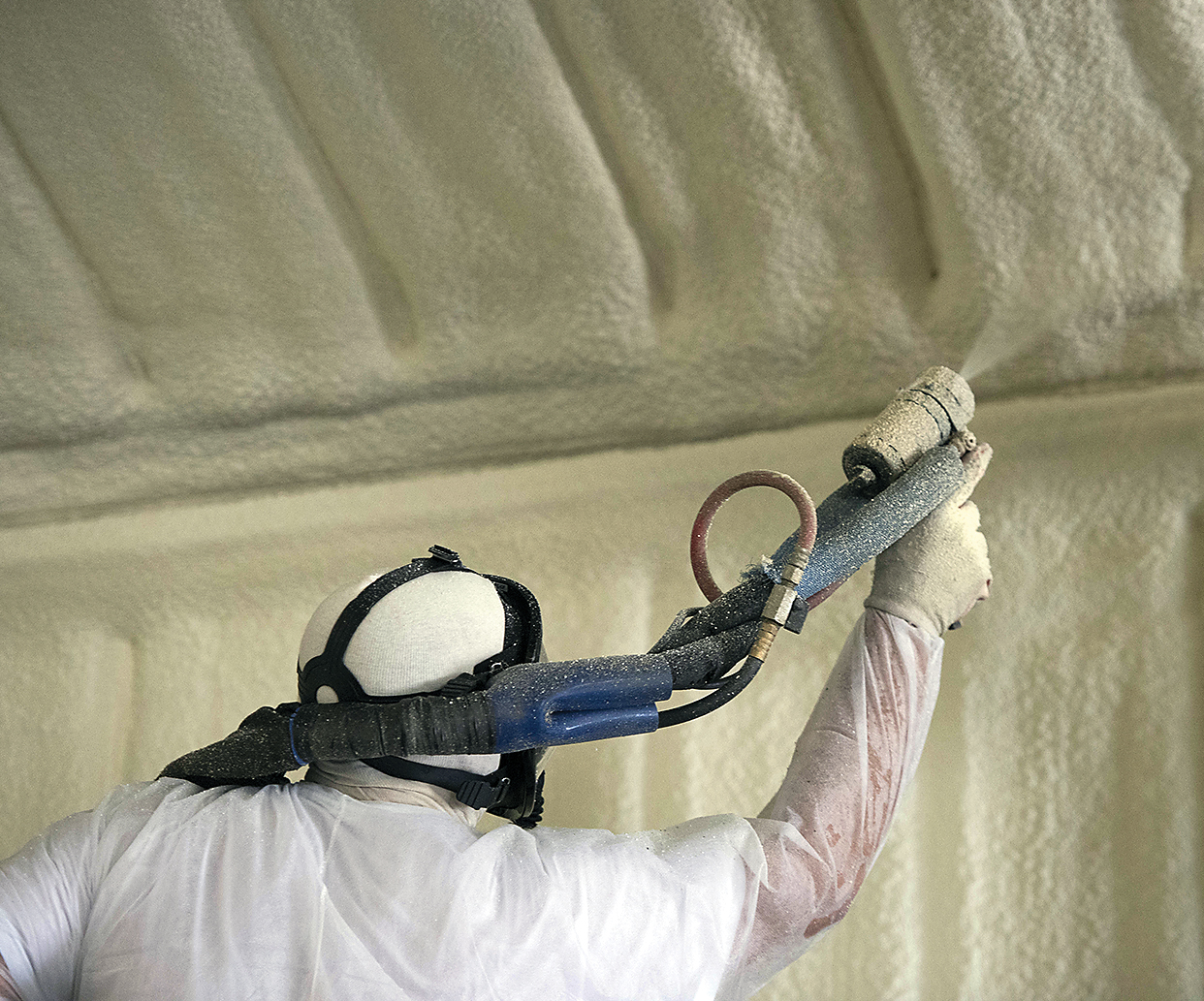 worker spraying SPF spray foam in building wearing proper PPE