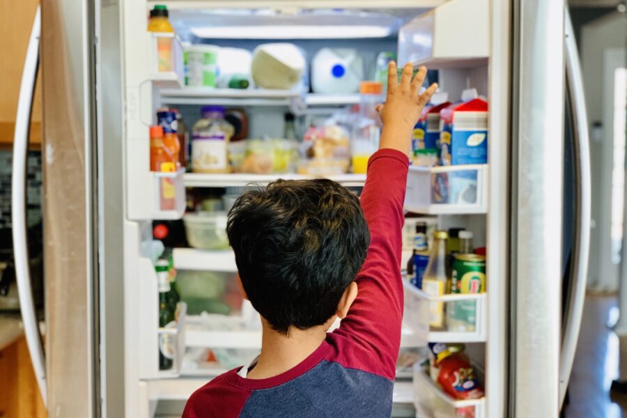 boy standing in front of refrigerator stocked with fresh food