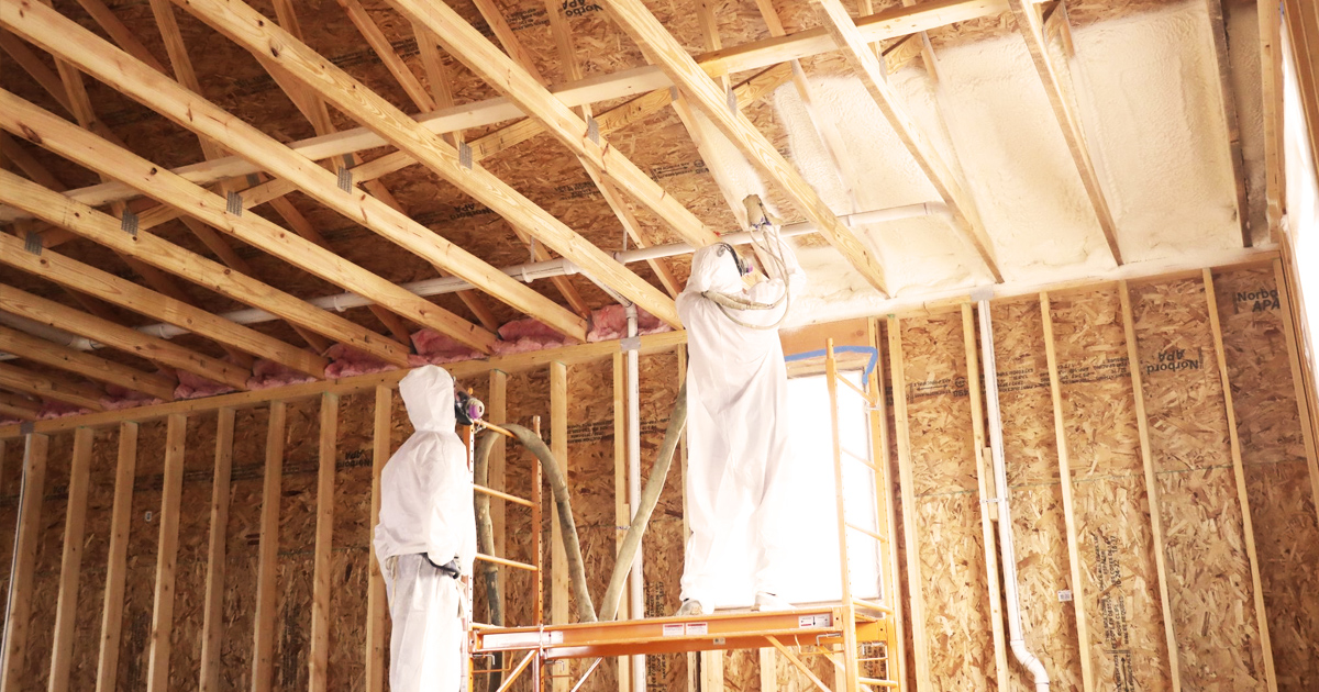 two spray foam contractors apply polyurethane spray foam insulation to ceiling rafters inside of house